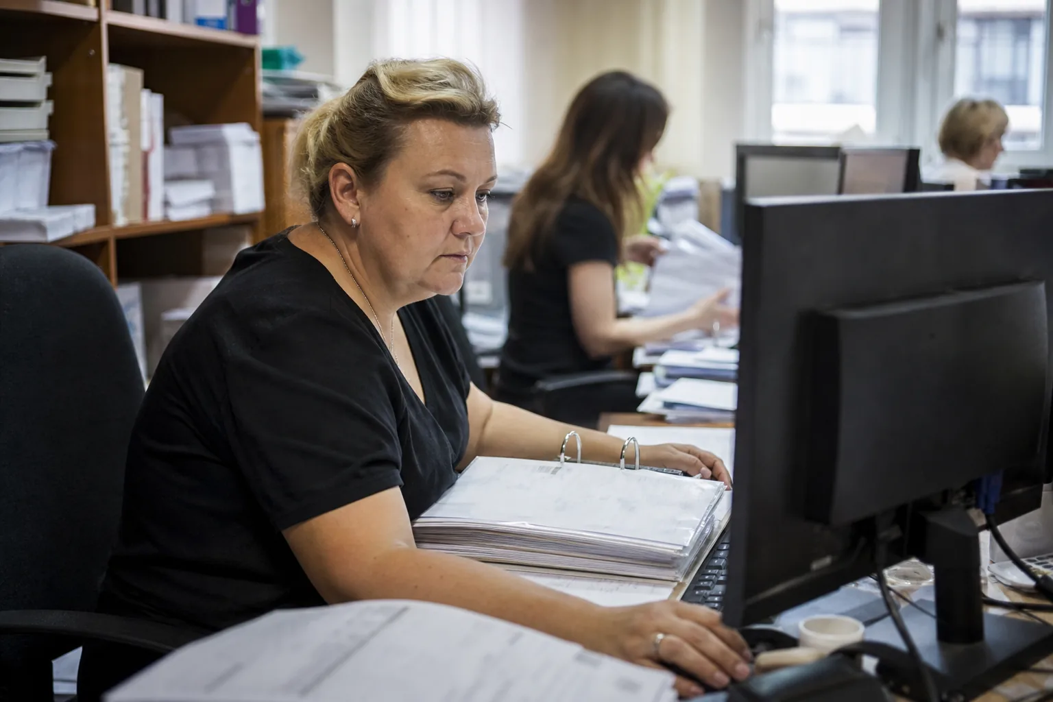 Główna księgowa w biurze firmy sprawdza na monitorze fakturę kosztową czekającą na akceptację kierownika